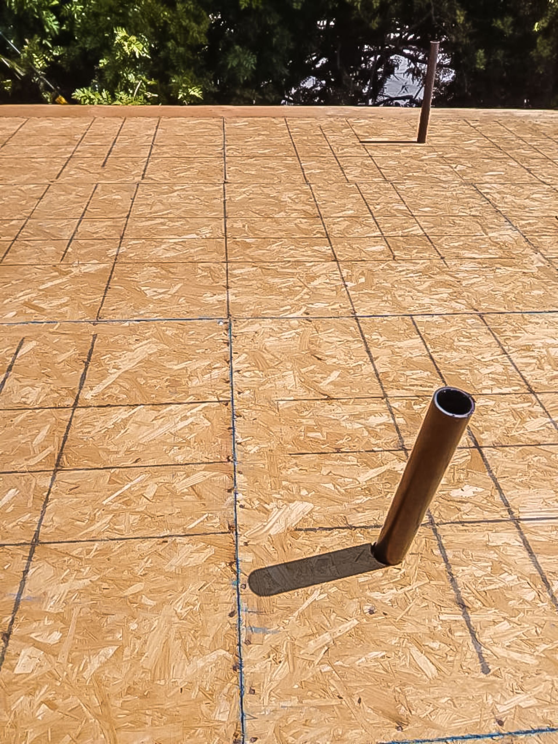 OSB roof sheathing with a black vent pipe protruding near the edge under construction
