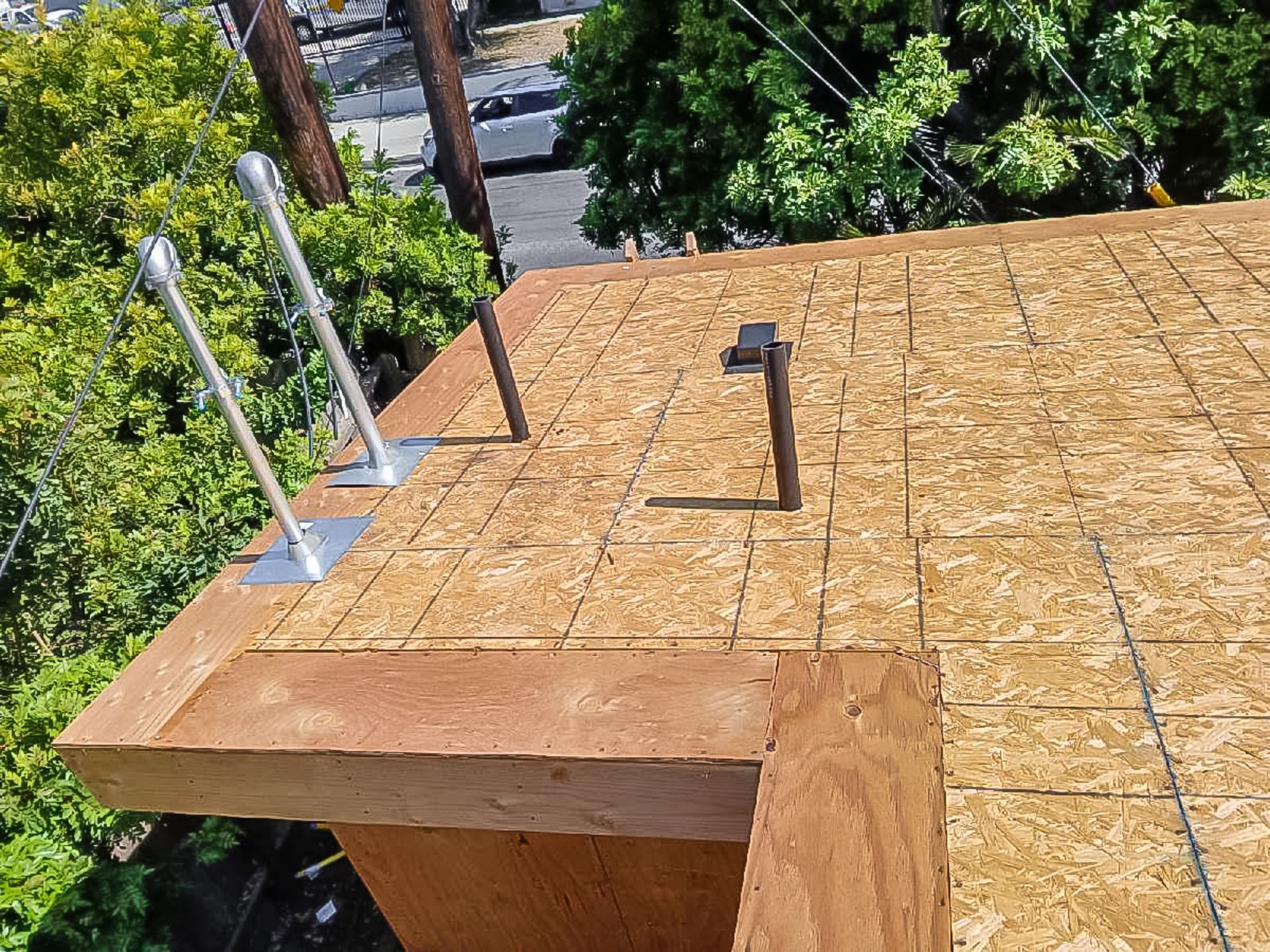 Rooftop with tan shingles, skylight vents, and metal railings beside trees and a street below