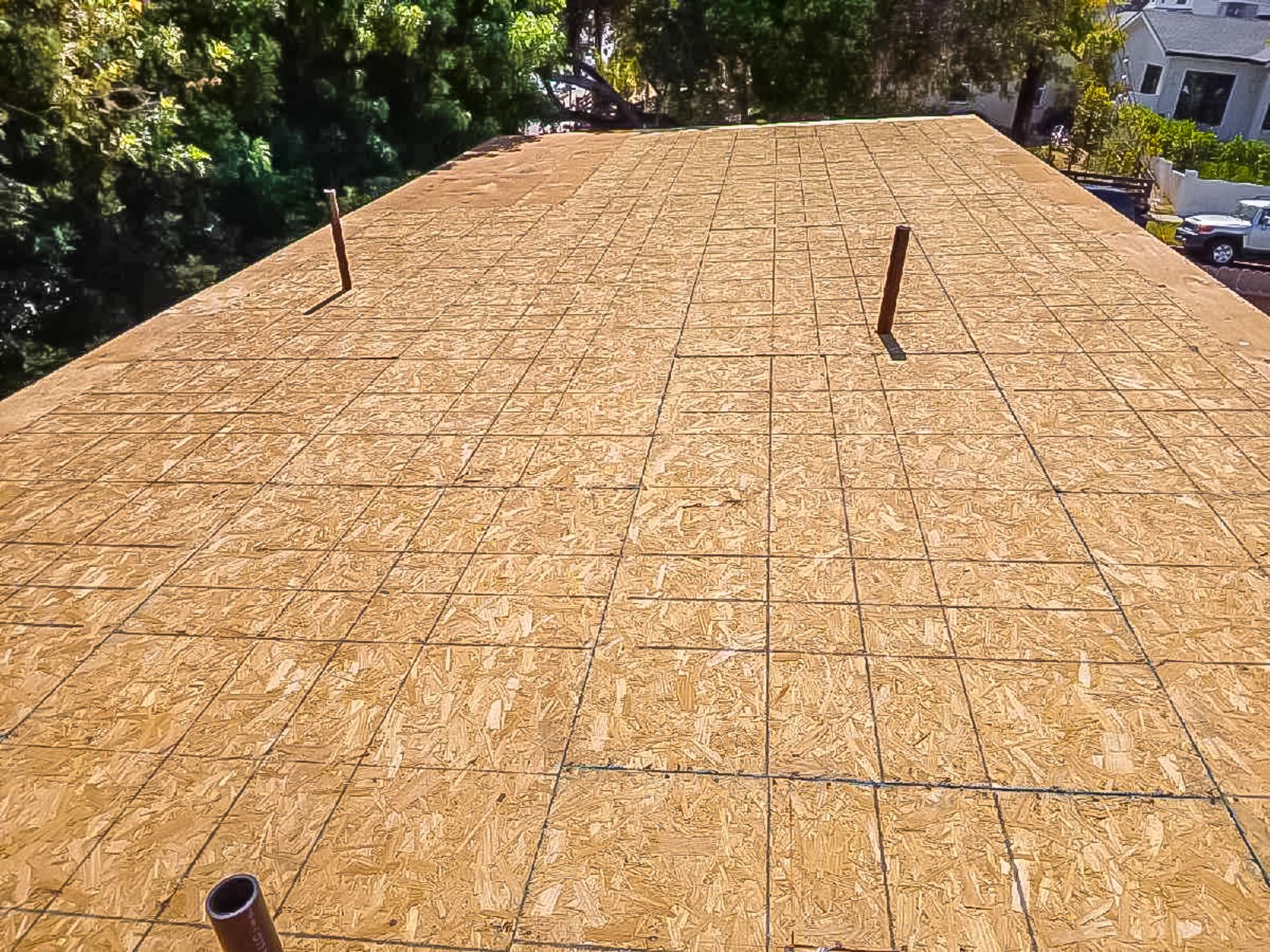 Freshly installed plywood roof sheathing with visible vents, surrounded by trees and nearby houses