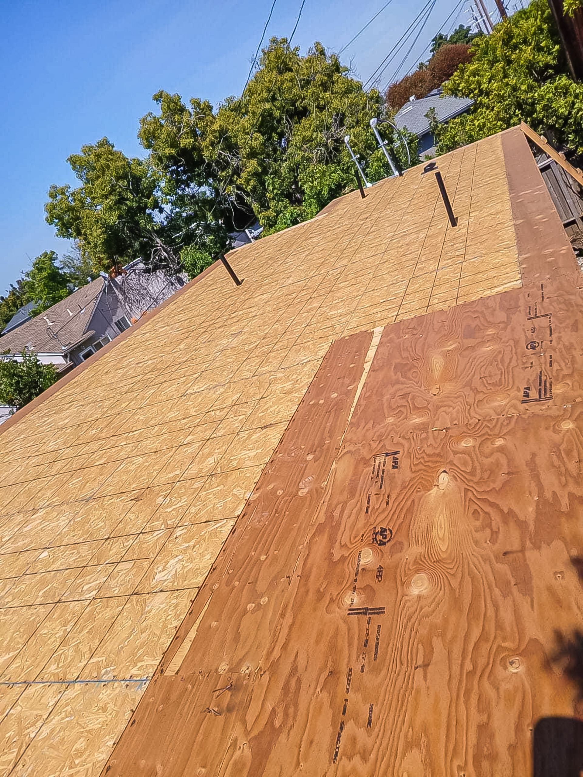 Partially covered house roof with OSB sheathing and a steep plywood panel under a blue sky