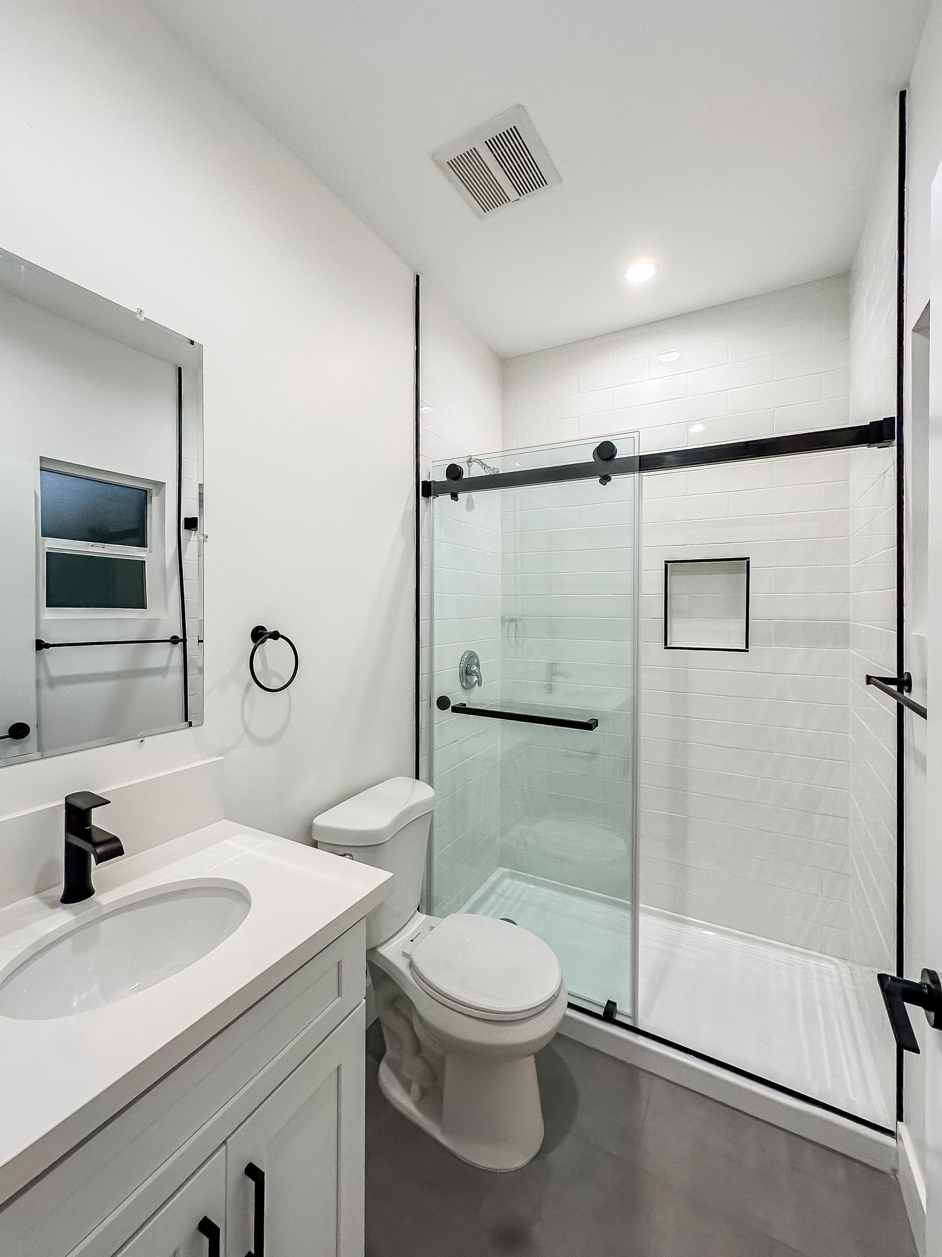 Bright white bathroom with sink vanity, toilet, and glass walk-in shower with black hardware.