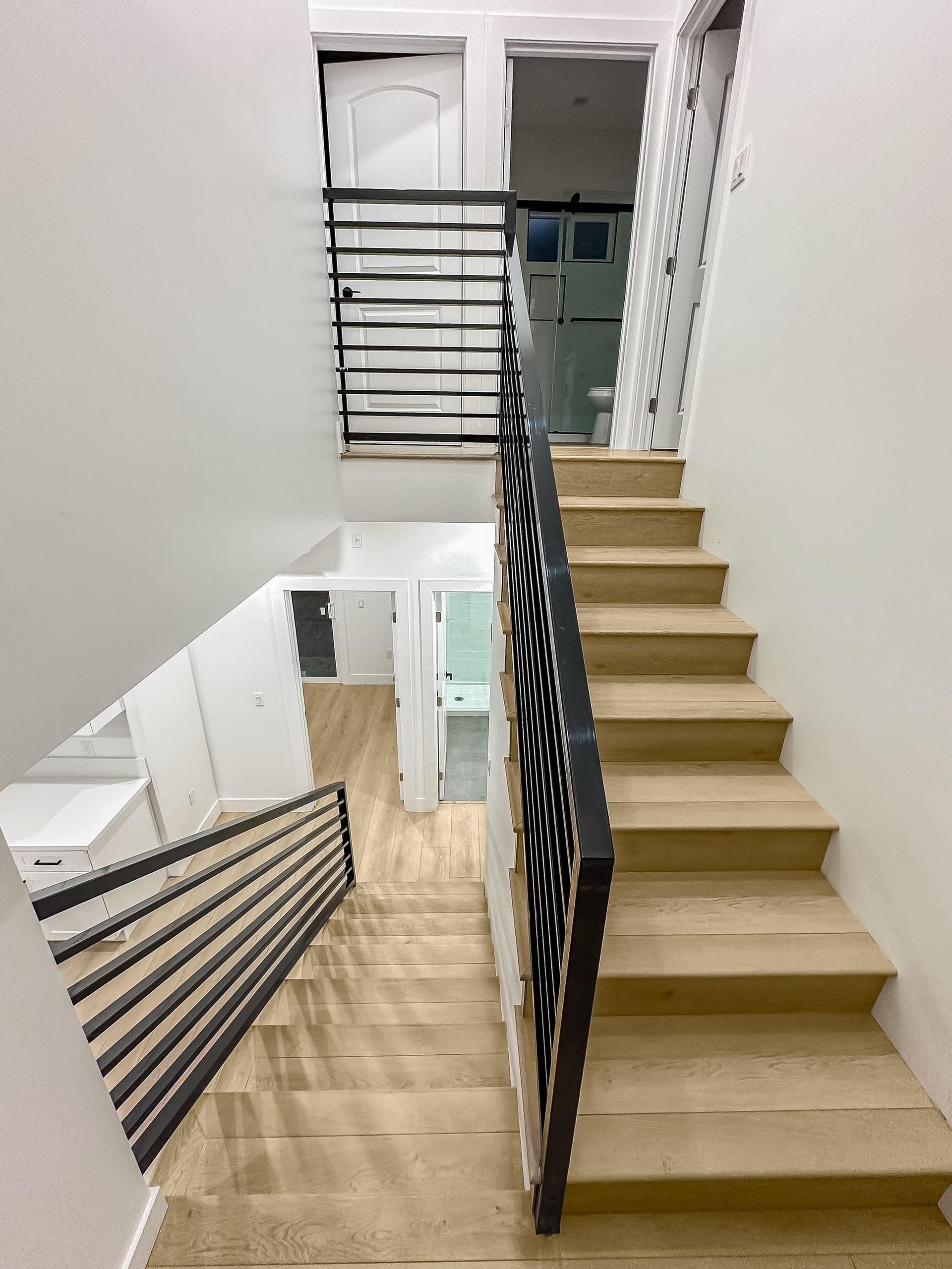 Modern indoor stairwell with beige steps, black railing, and white walls, viewed from above and below