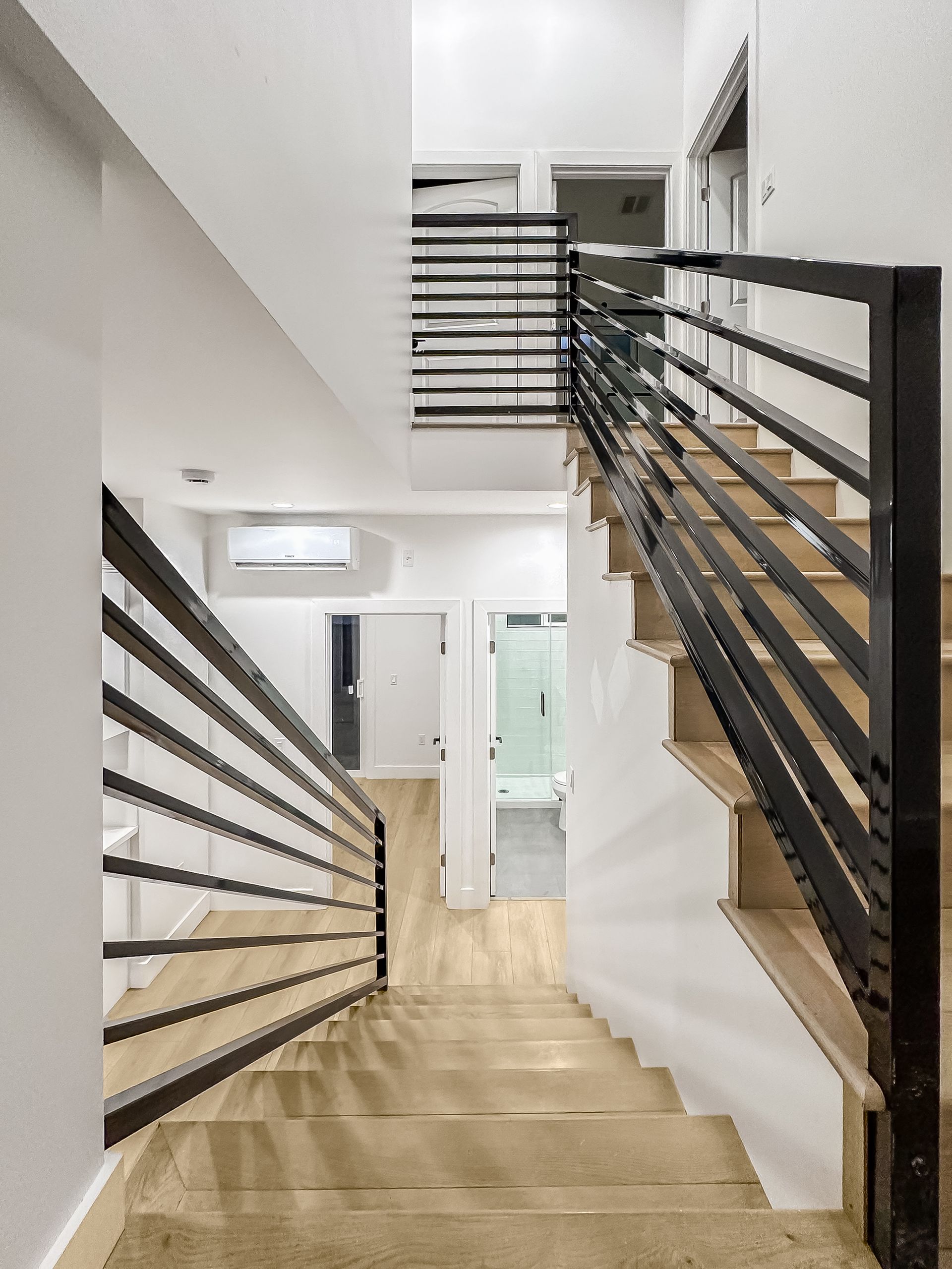 Modern stairwell with wood steps, black railings, and white walls leading to a bright interior landing