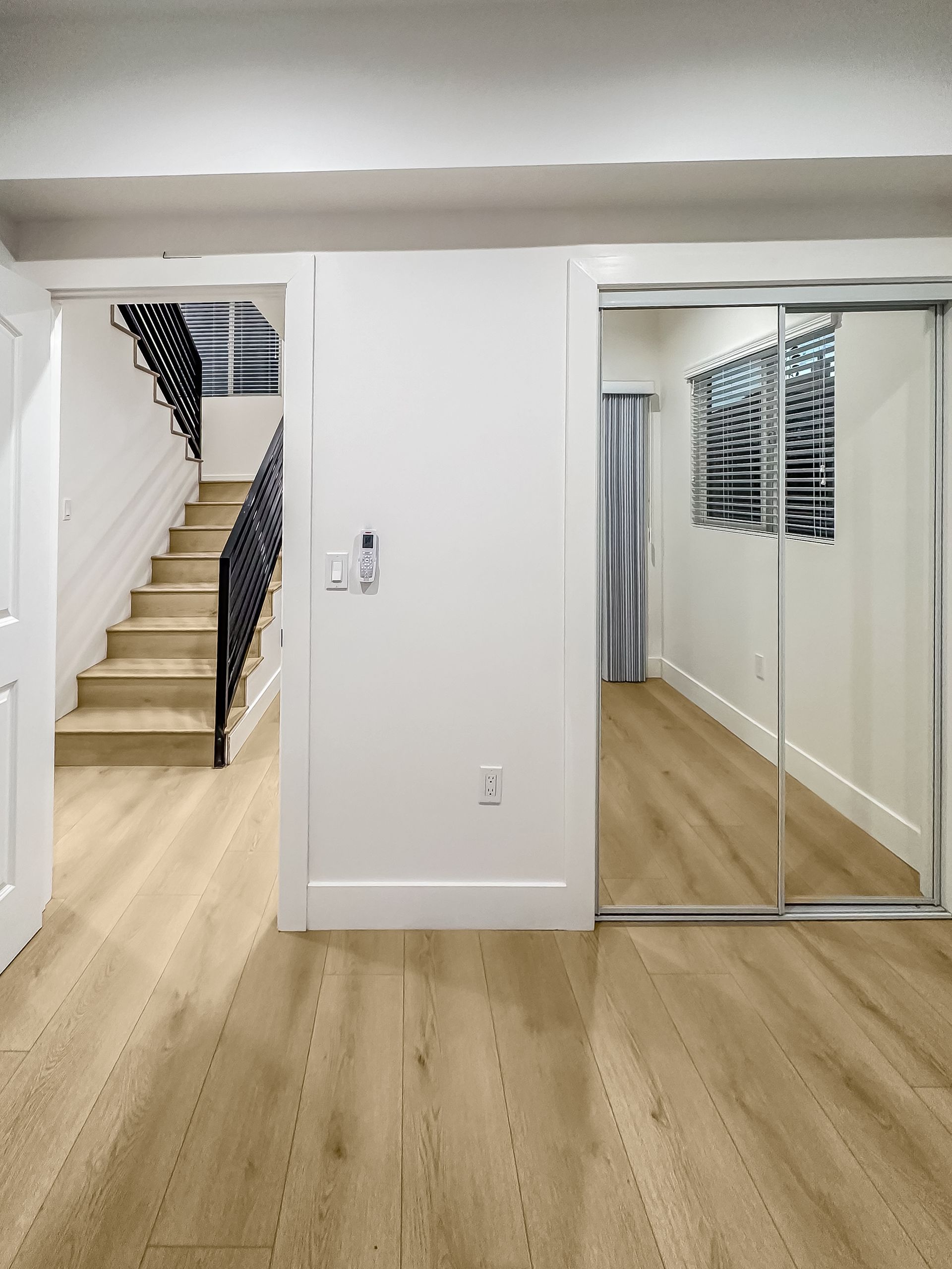 Bright hallway with stairs on the left, mirrored closet doors on the right, and light wood flooring.