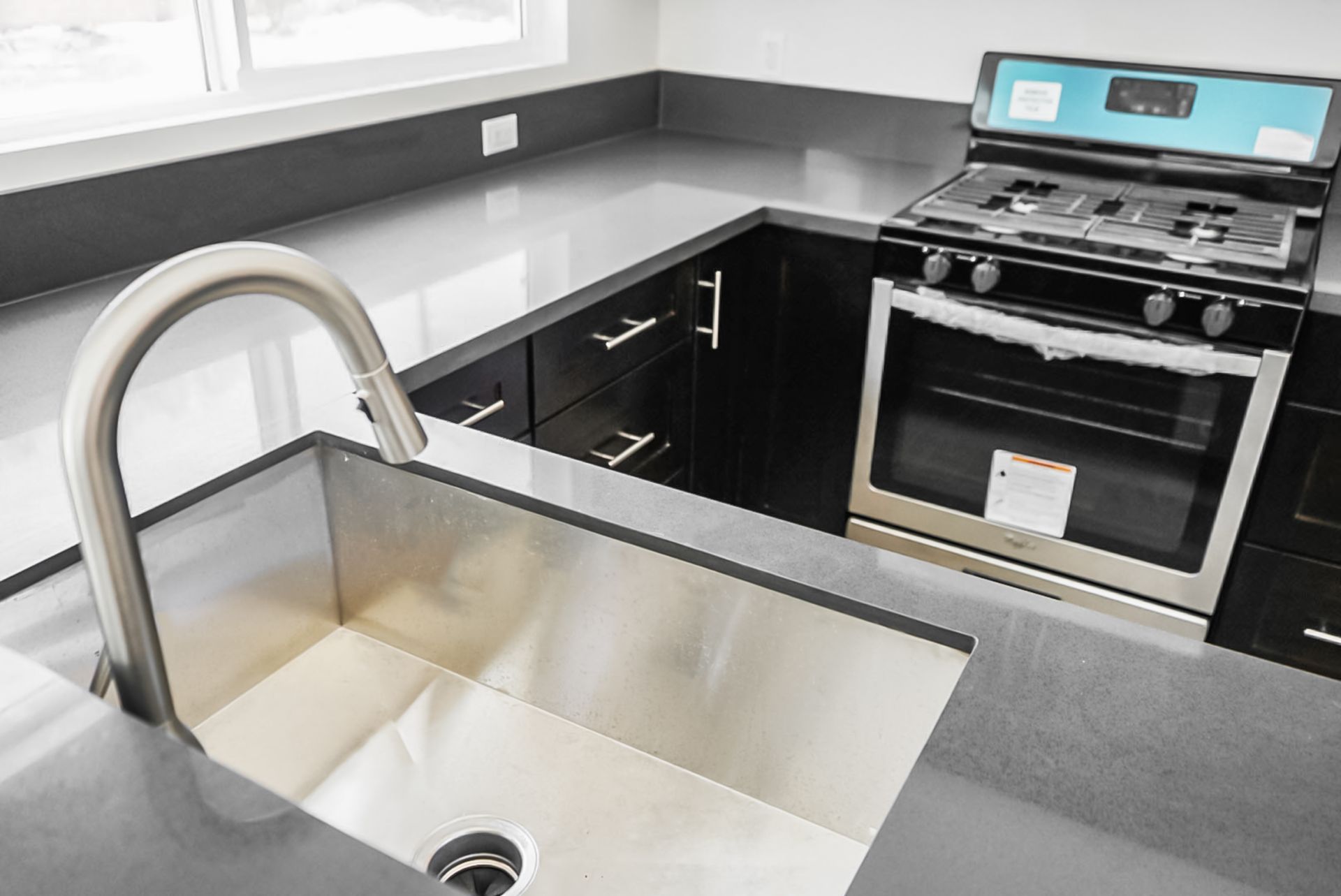 Modern kitchen with stainless steel sink, black countertops, and a stainless steel stove by a window