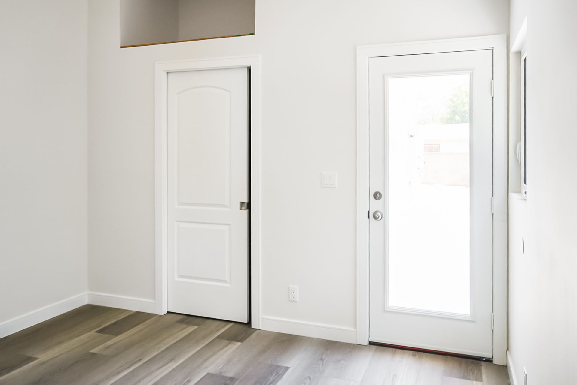 Bright empty room with two white doors and light wood flooring
