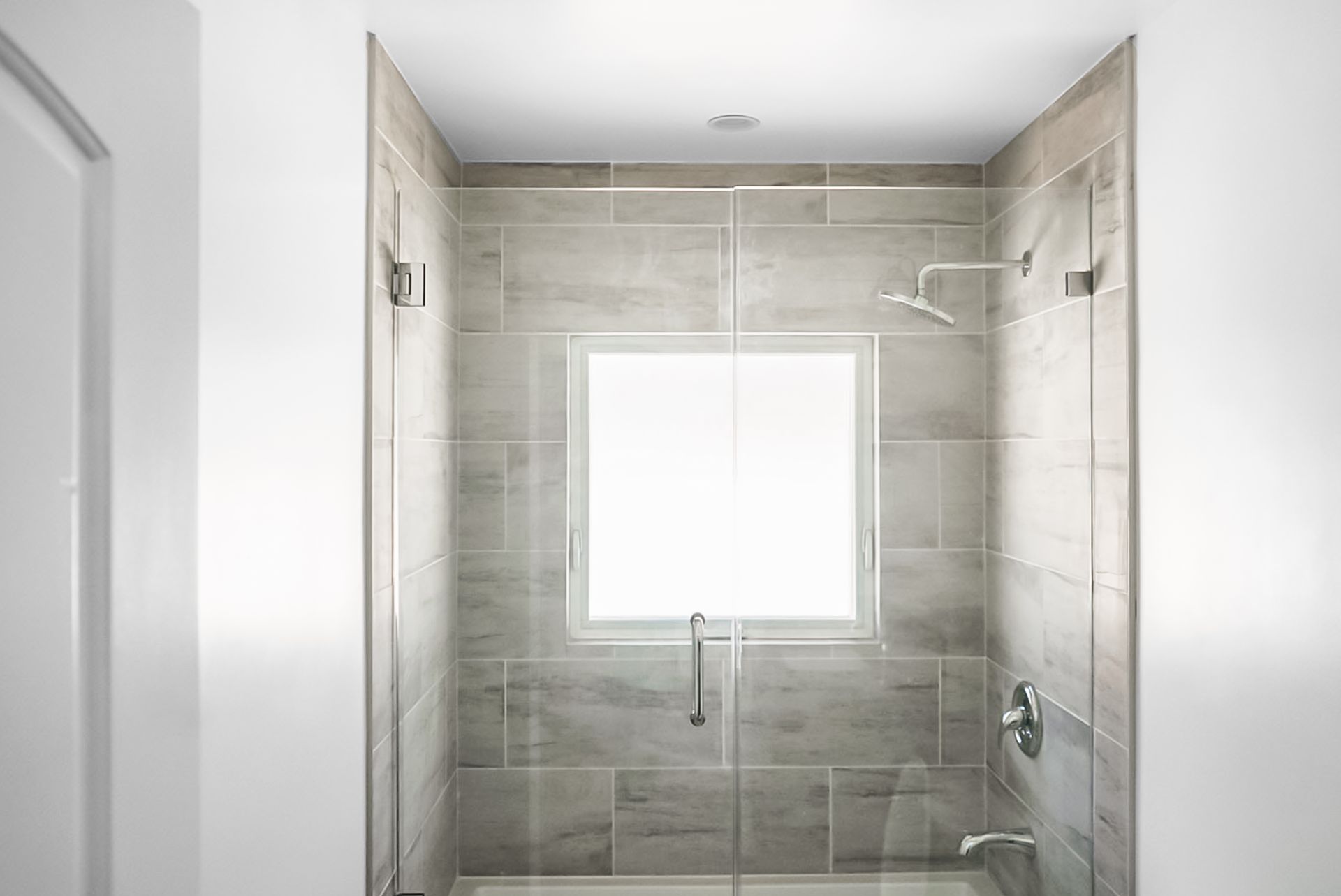 Small tiled walk-in shower with a window and chrome fixtures, viewed from the bathroom doorway