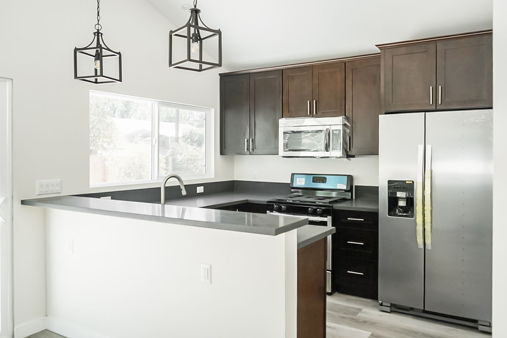 Modern kitchen with stainless steel appliances, dark cabinets, and a white island under pendant lights