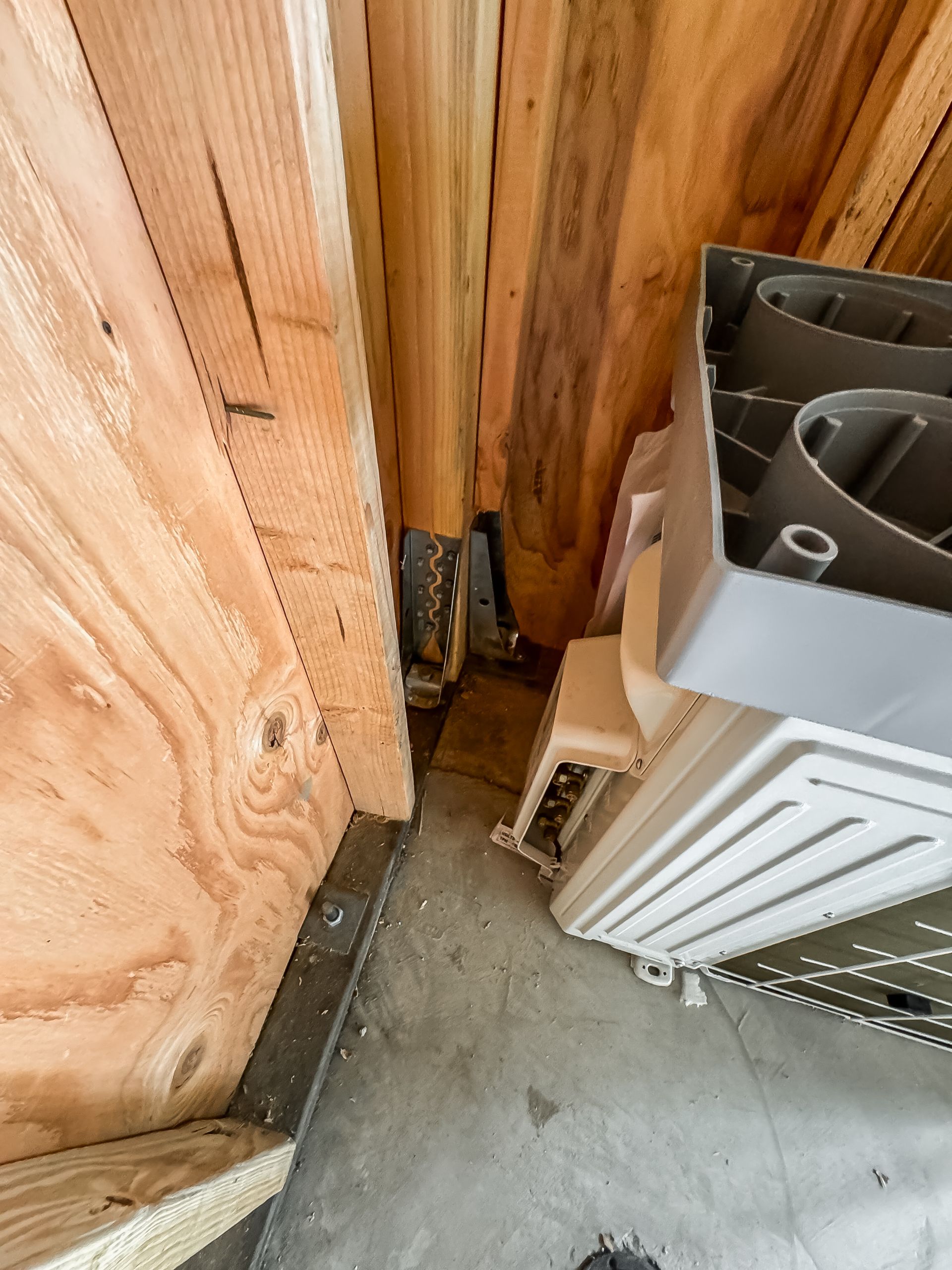 Narrow corner of a garage with plywood wall, exposed plumbing, and a white radiator on a concrete floor