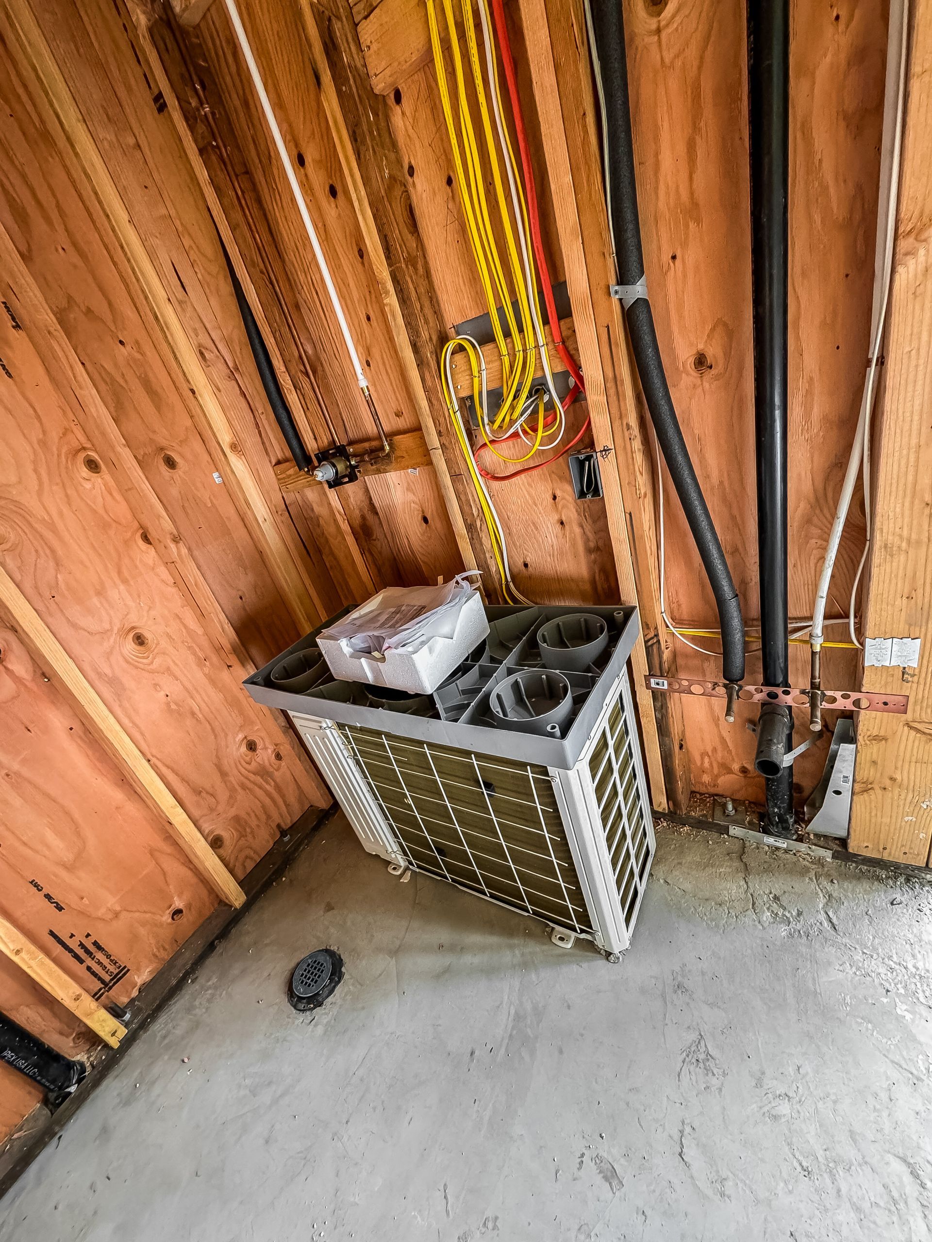 HVAC unit in a wood-framed utility closet with exposed wiring and concrete floor