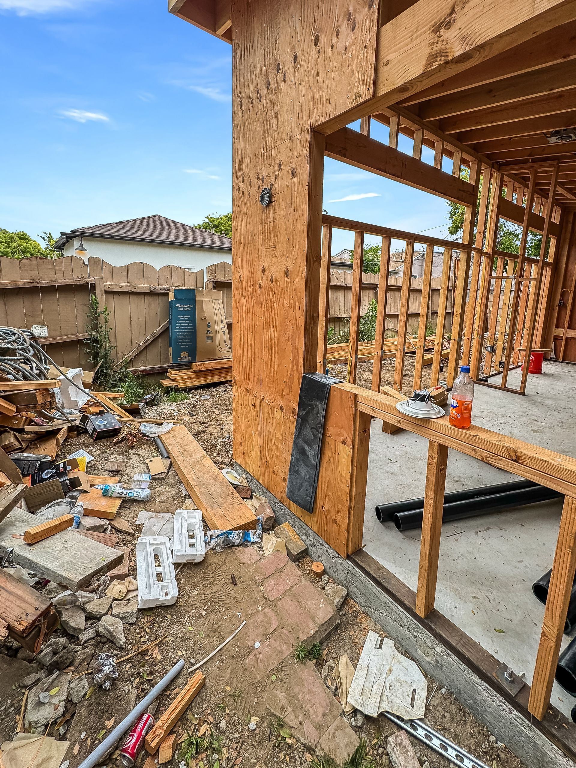Partially framed house under construction with debris and building materials in a backyard