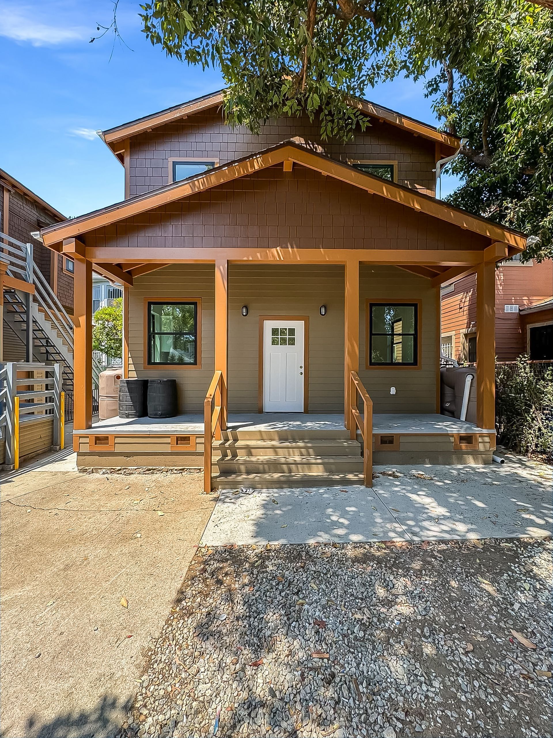 Small wooden house with front porch, white door, and gravel path under a tree