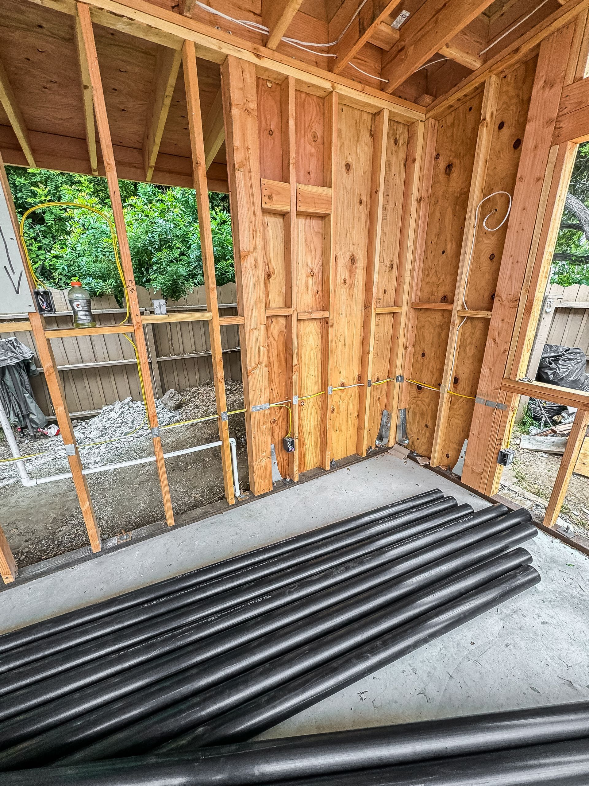 Framed interior of a building under construction with concrete floor and stacked black pipes.