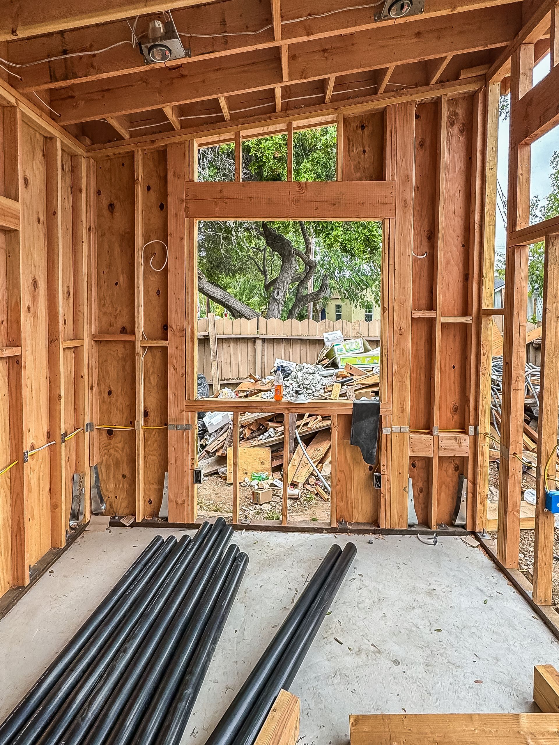 Wood-framed room under construction with concrete floor, exposed studs, and materials stacked near a window opening