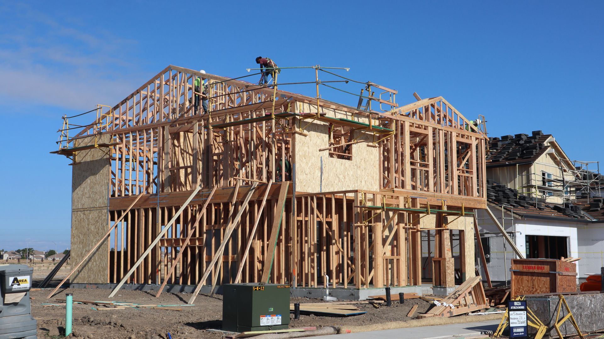 Wood-framed house under construction with exposed beams and roof trusses in a residential neighborhood