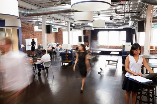 A group of people are standing and walking in a large room.