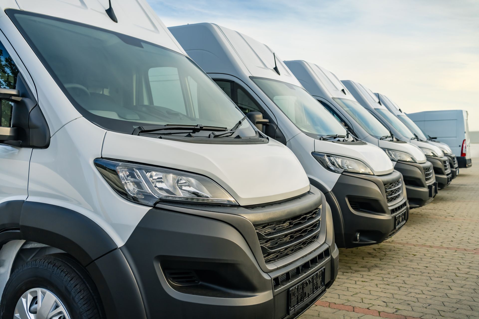 Row of white delivery vans parked in a lot, angled toward the camera.