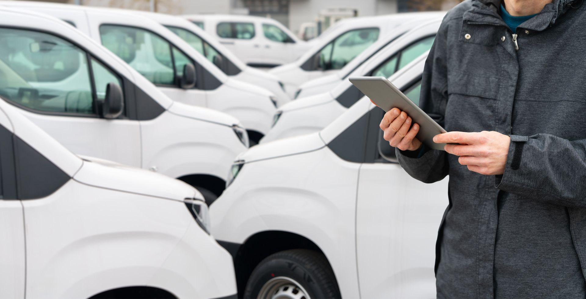 Person holding a tablet beside a row of white vans in a parking lot