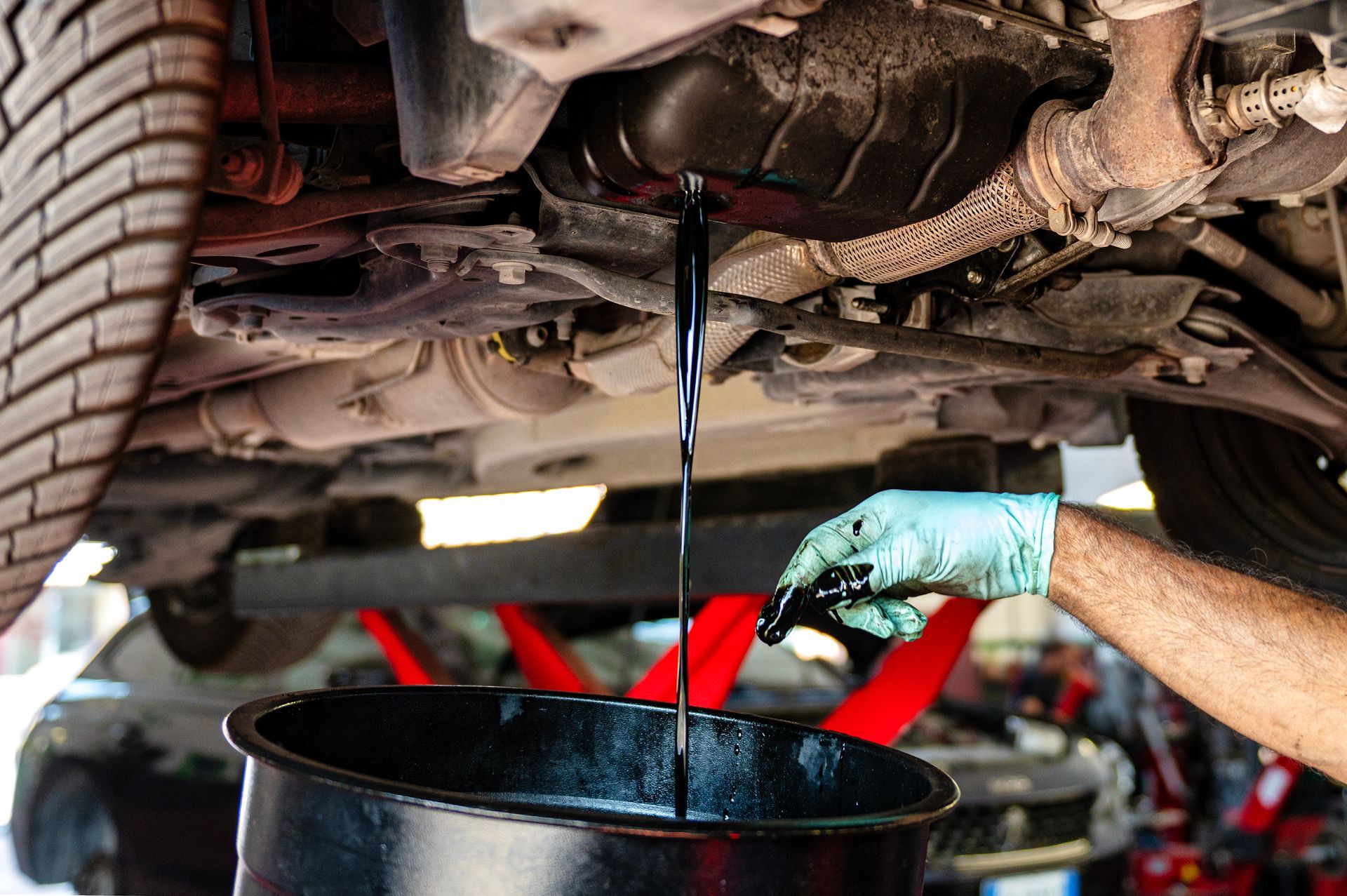 Mechanic draining dark oil from a car into a black pan under the vehicle