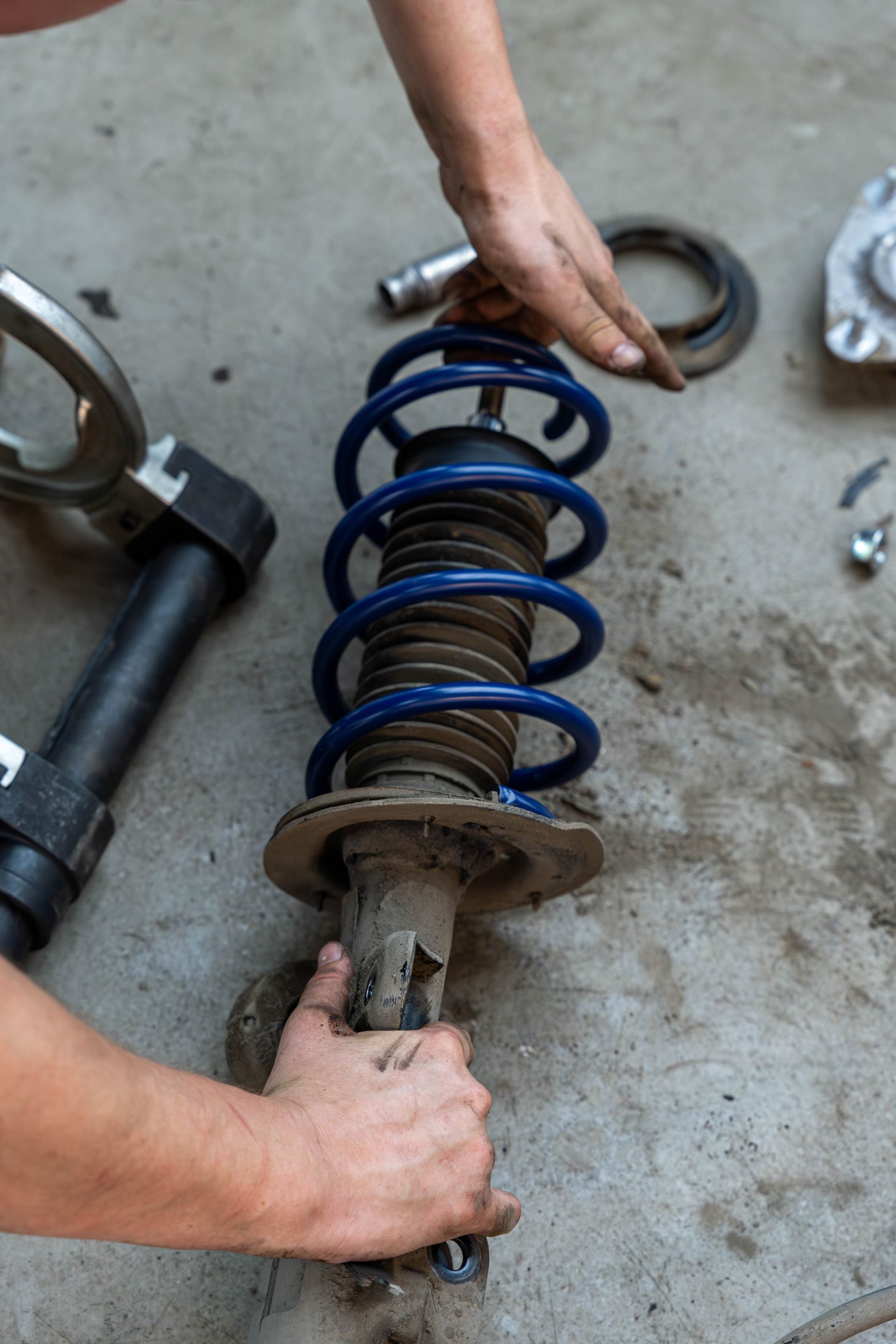 Hands holding a blue coil spring shock absorber on a concrete floor.