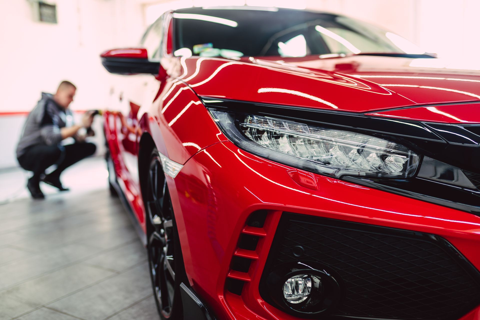 Red sports car close-up in a showroom, with a person crouching in the background