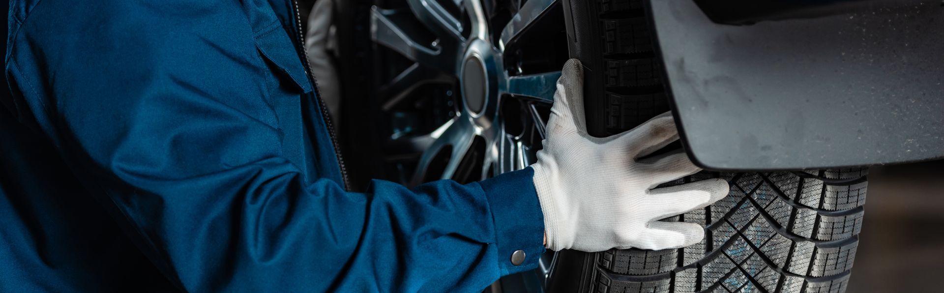 Mechanic in blue jacket inspecting a car tire and wheel