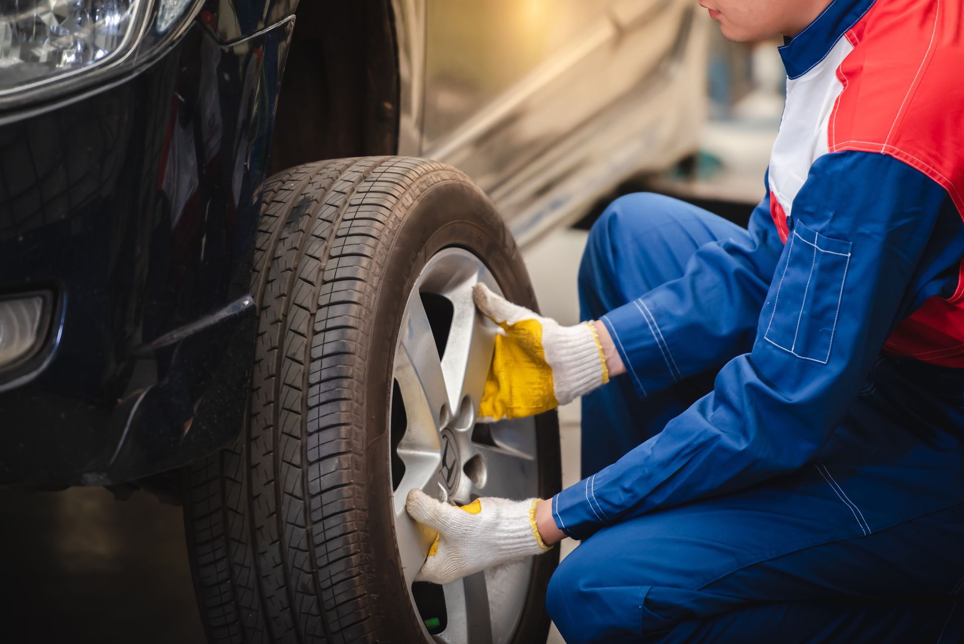 Mechanic in blue overalls and yellow gloves changing a car tire with a wrench