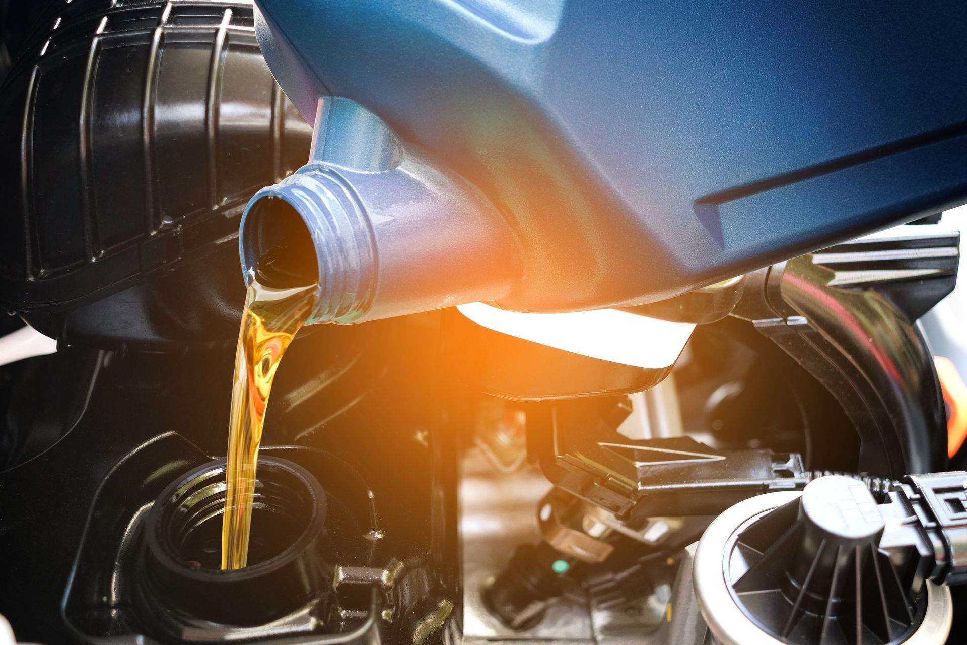 Oil pouring from a car engine into a black container, close-up with warm sunlight.