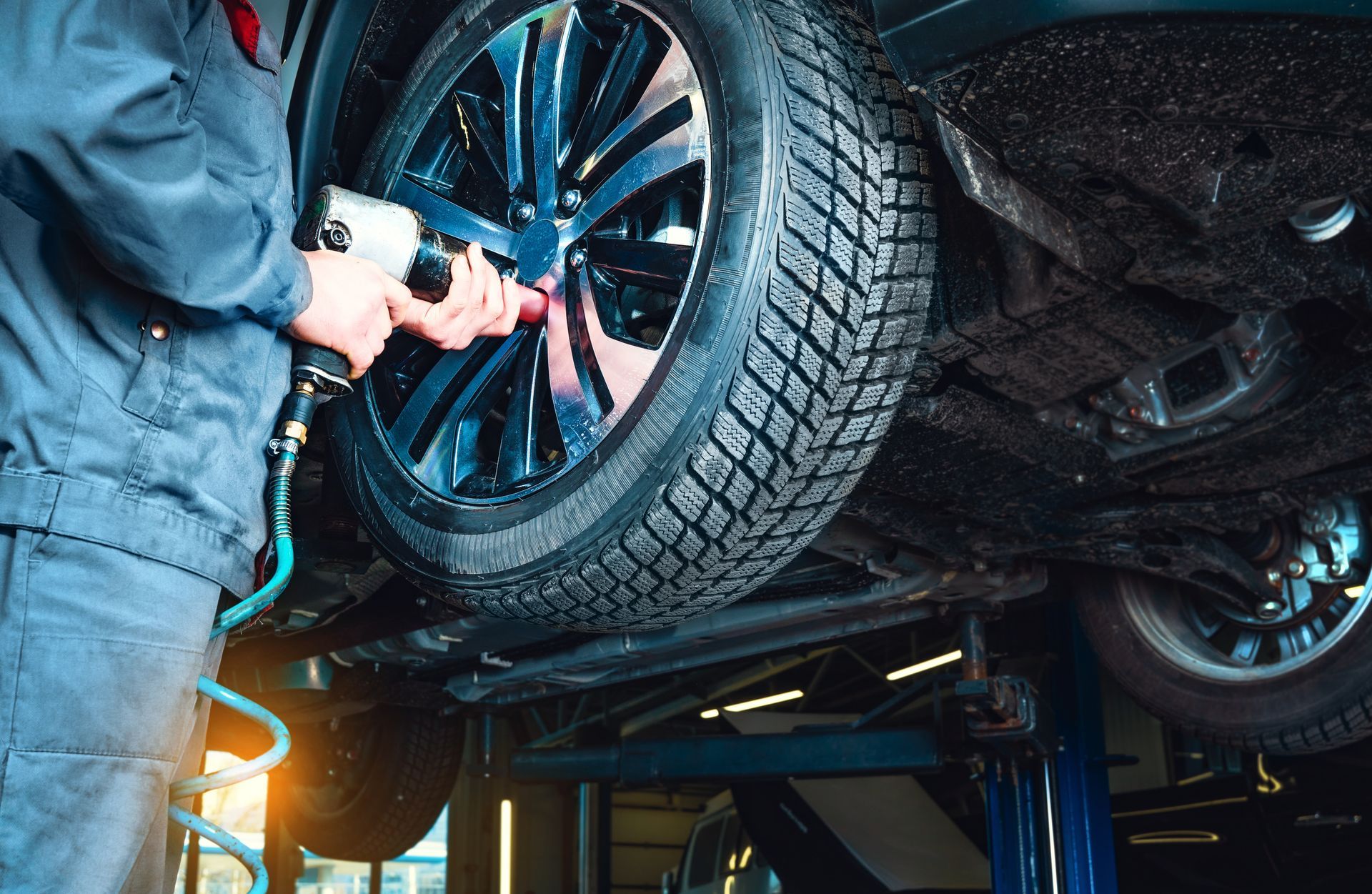 Mechanic changing a tire on a car lifted in a garage, with a blue wheel and winter tire.