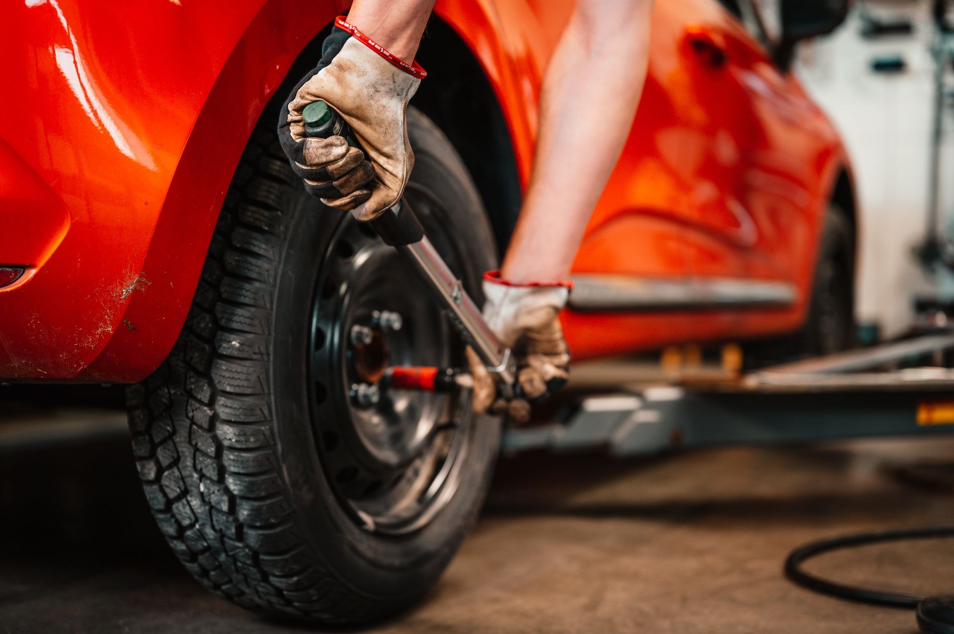 Mechanic tightening a wheel lug on a red car with a wrench in a garage