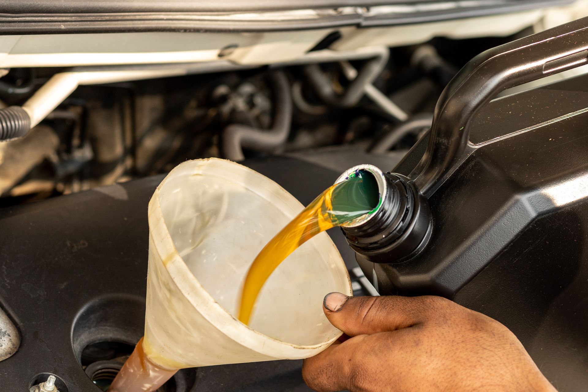 Oil being poured from a car into a funnel over a container in the engine bay.