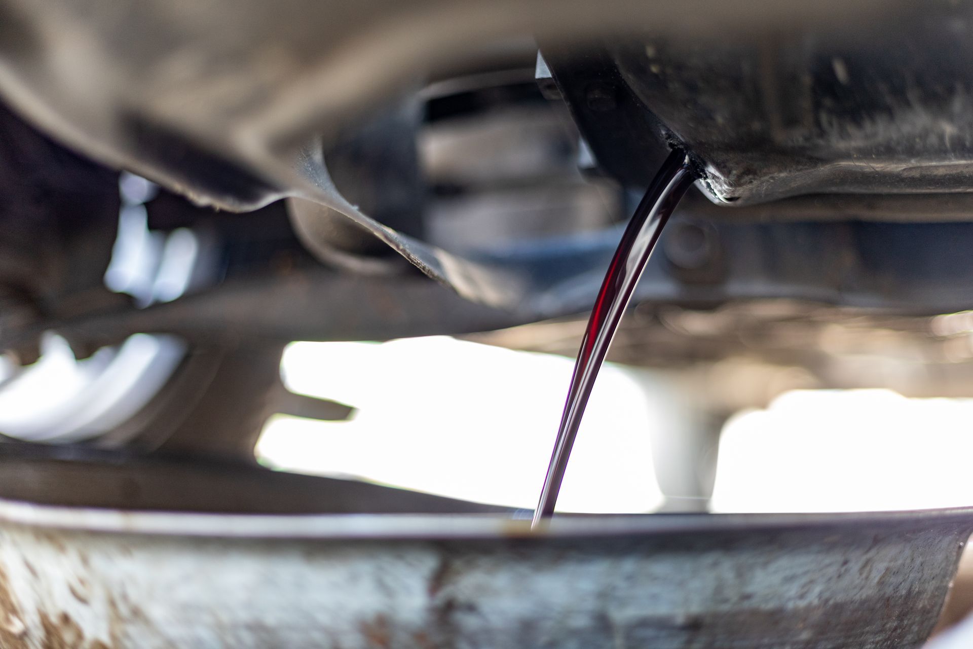 Close-up of dark liquid dripping from an underside pipe into a metal container