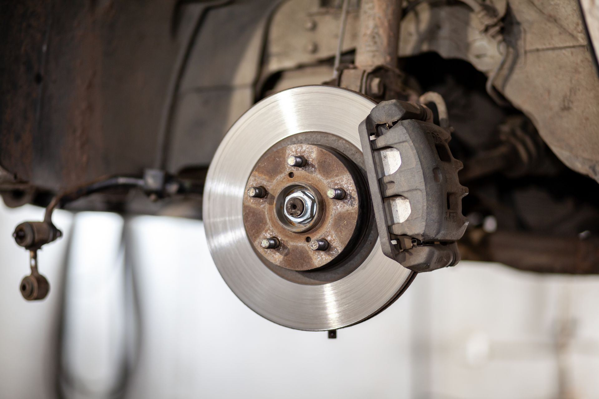 Car brake rotor and caliper exposed with wheel removed in a garage undercarriage view
