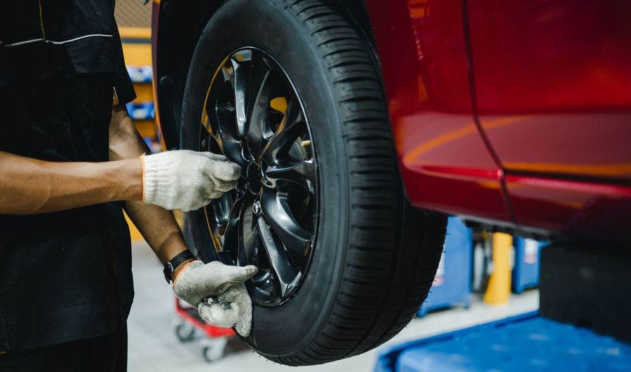 Mechanic wearing gloves tightening lug nuts on a red car’s front wheel in a repair shop