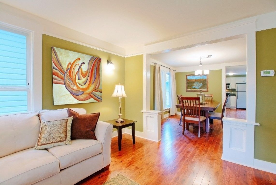 Bright living-dining room with white sofa, abstract wall art, wood floors, and a table by a window
