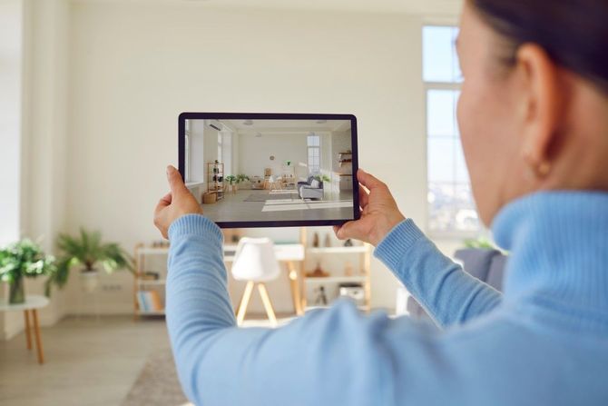 Person holding a tablet showing a bright living room interior with furniture and plants