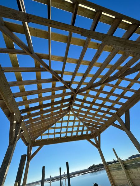 Wooden pergola over a waterfront walkway under a bright blue sky