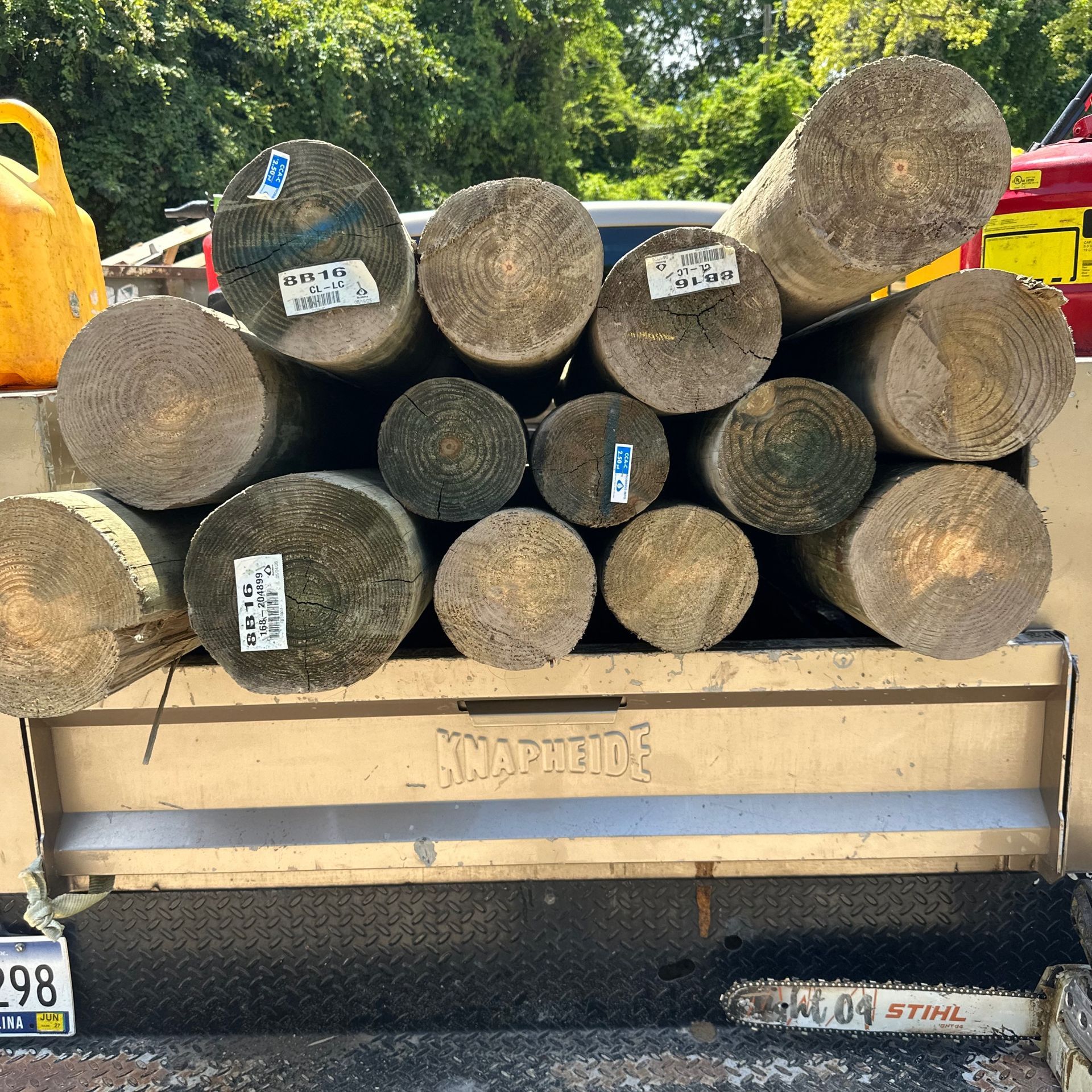 Stacked log rounds in the bed of a tan utility truck outdoors.