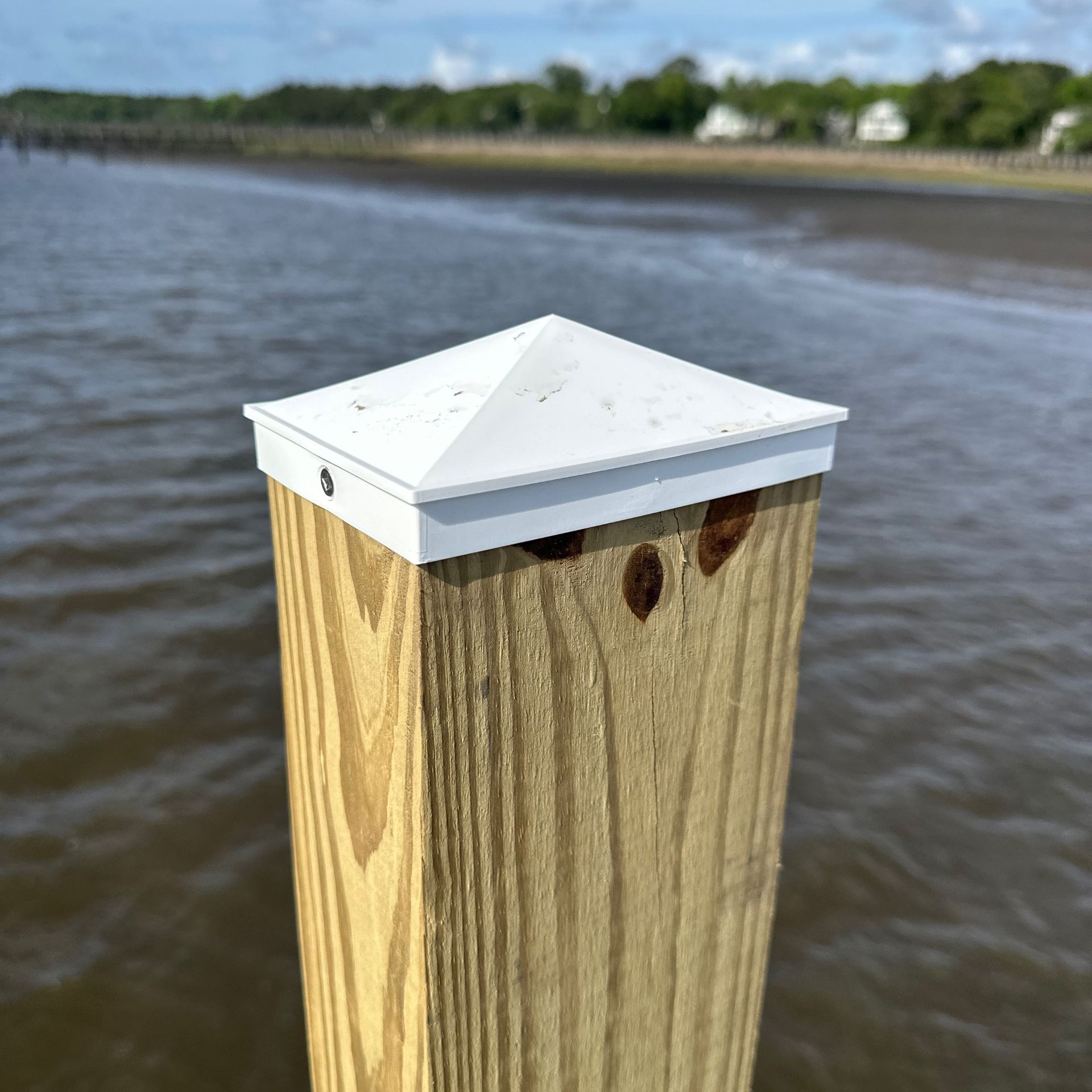 Wooden dock post with a white cap beside calm water under a blue sky