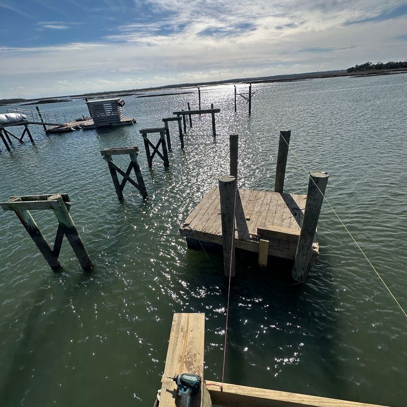 Sunlit marina with several wooden dock frames and platforms on calm, rippling water