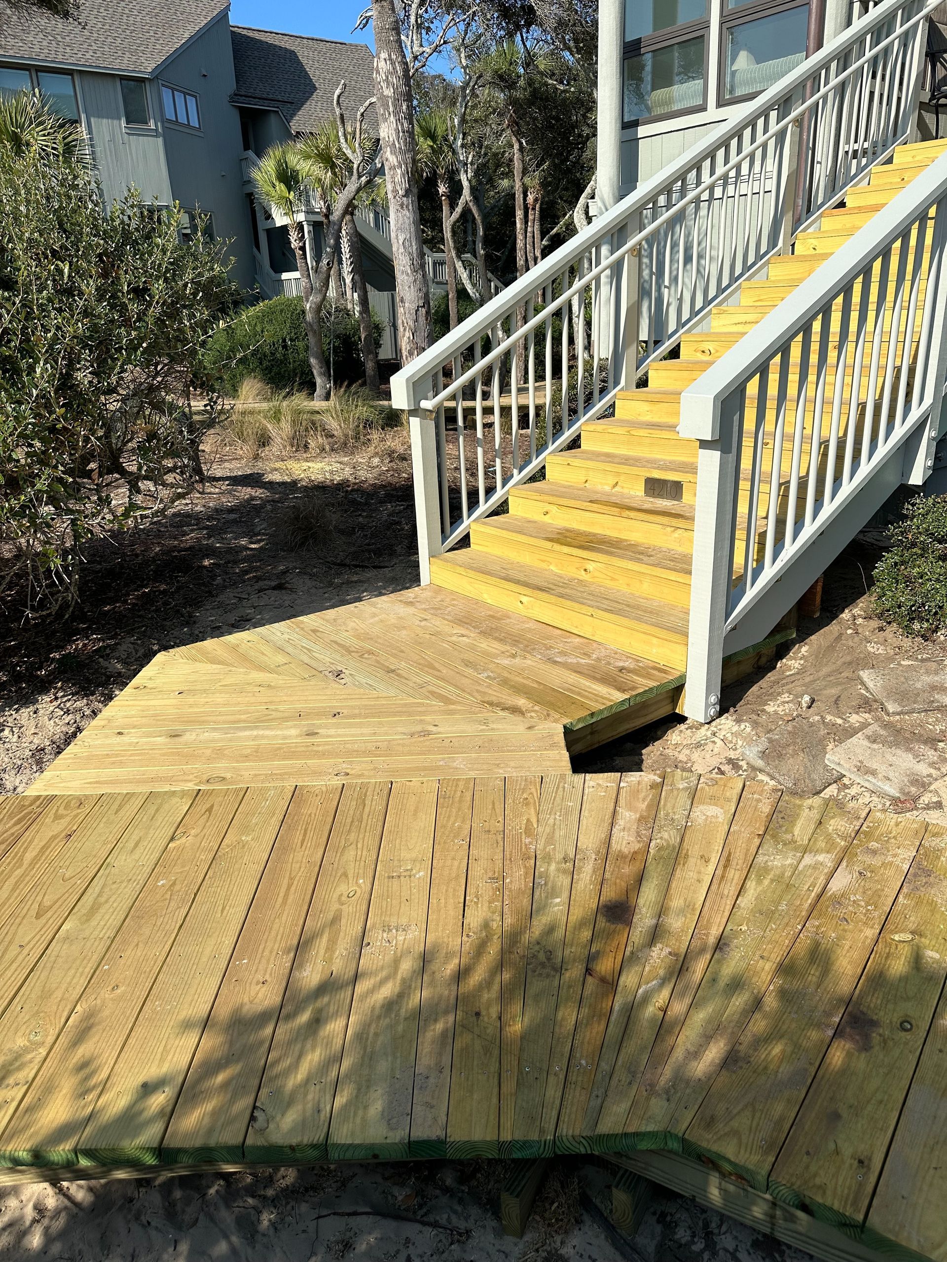Yellow wooden ramp and stairs with white railings leading to a house entrance.