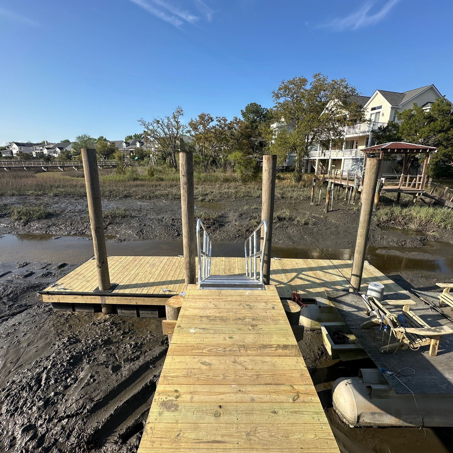 Wooden dock under construction at low tide beside muddy marsh and waterfront homes