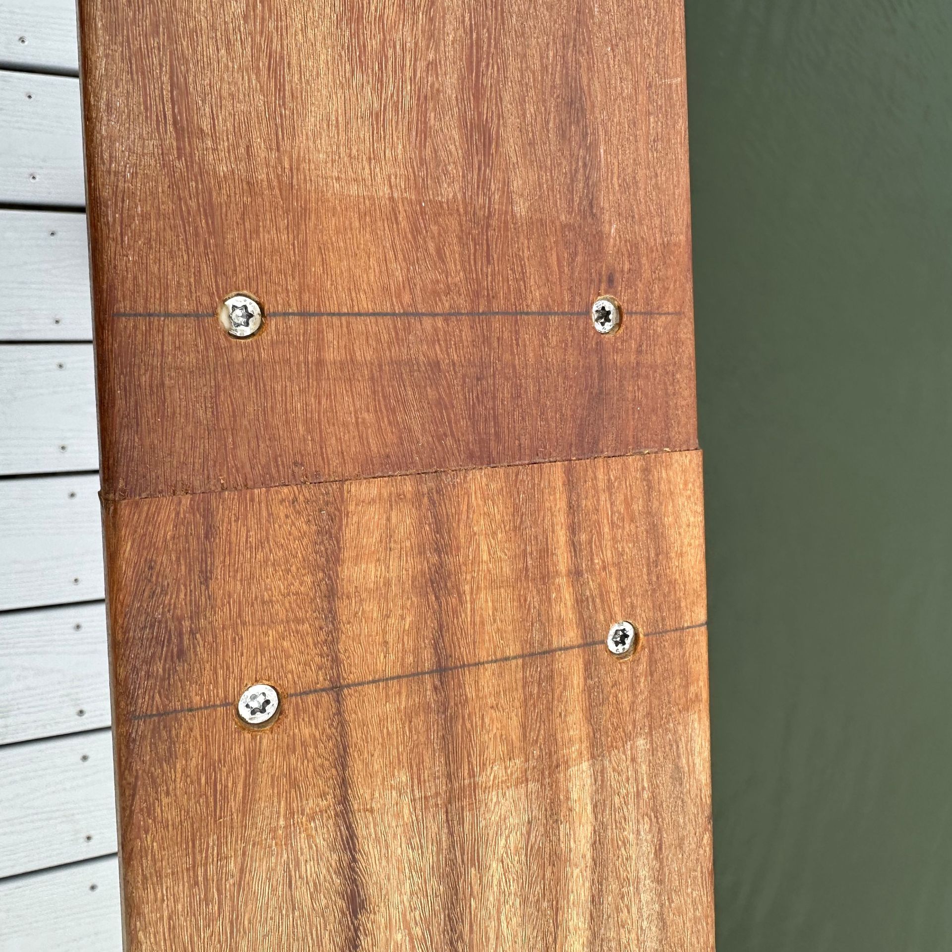 Close-up of a wooden board with four screws against a white wall and green surface