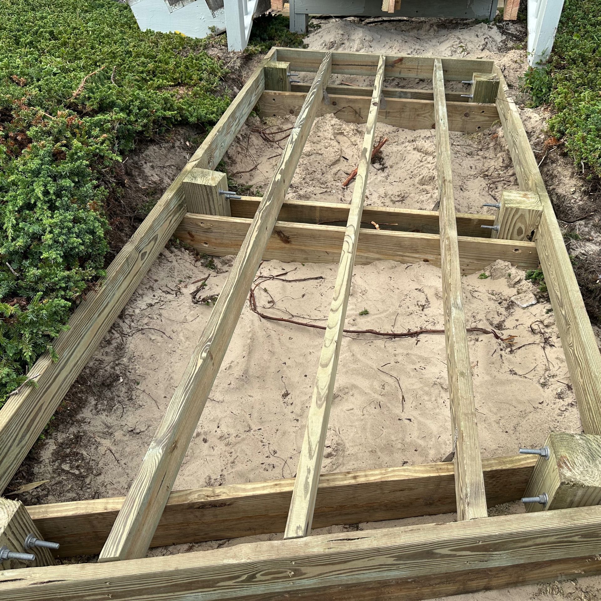Wooden frame for a sandy walkway or patio under construction beside a garden and house steps