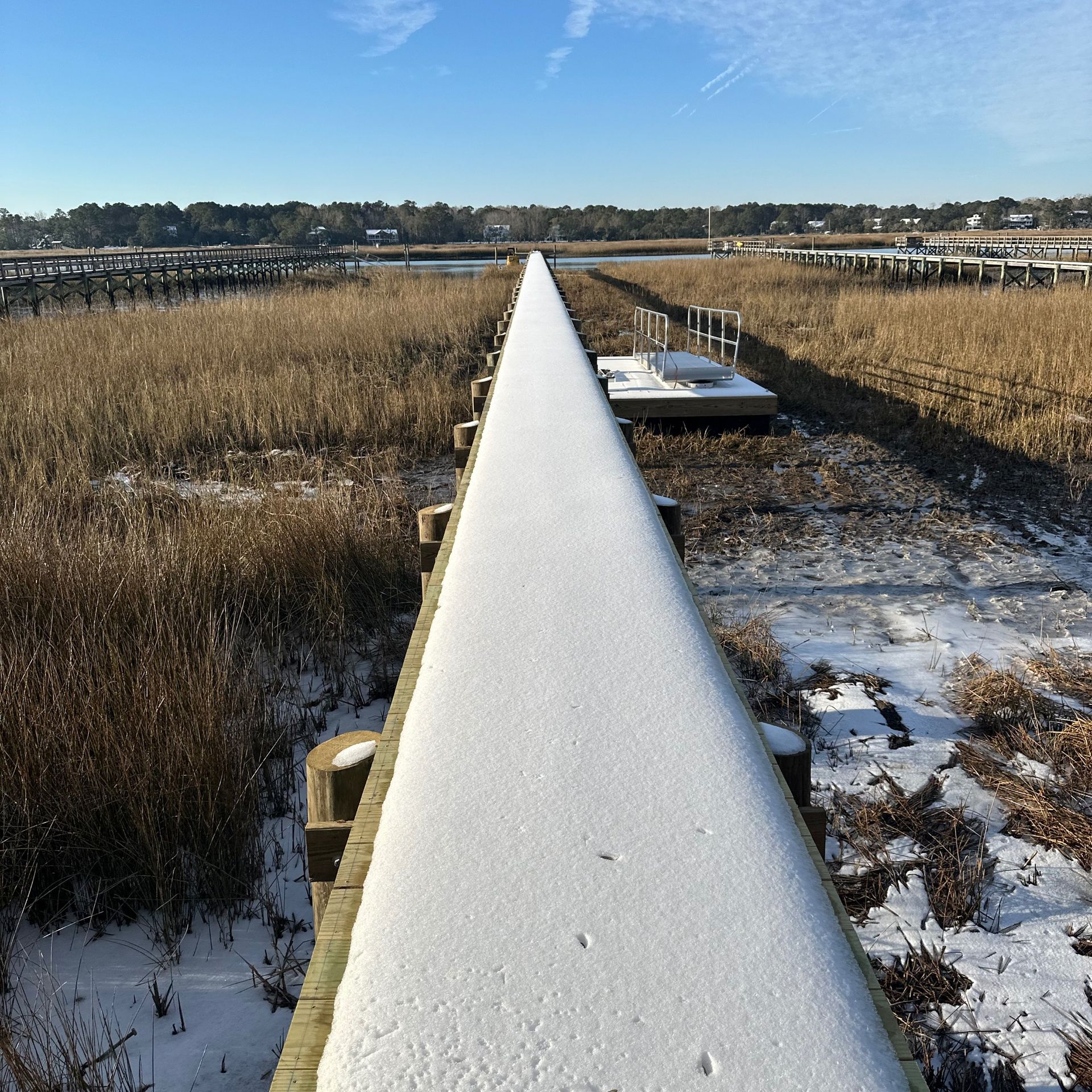 Snow-covered pipeline stretching through a marshy field under a clear blue sky.