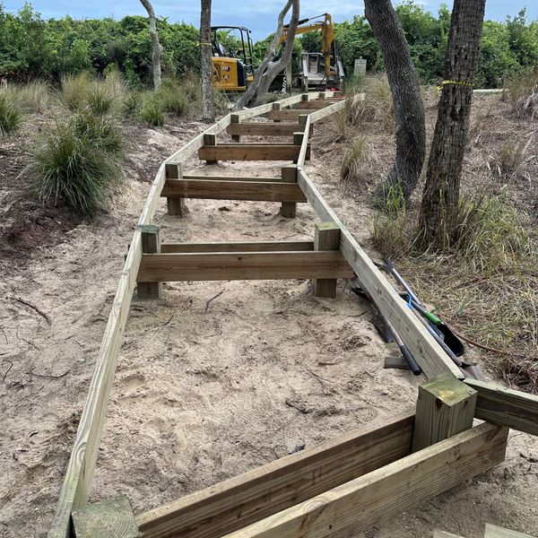 Sandy trail with wooden steps and railings winding through brush and trees under a clear sky
