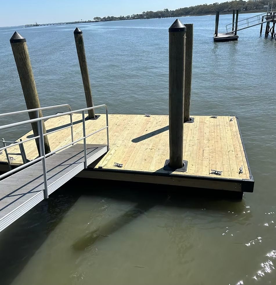 Small dock platform with black posts on calm water under a clear sky.