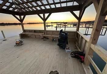 Empty wooden pavilion on a pier at sunset, overlooking calm water with benches and fishing gear.