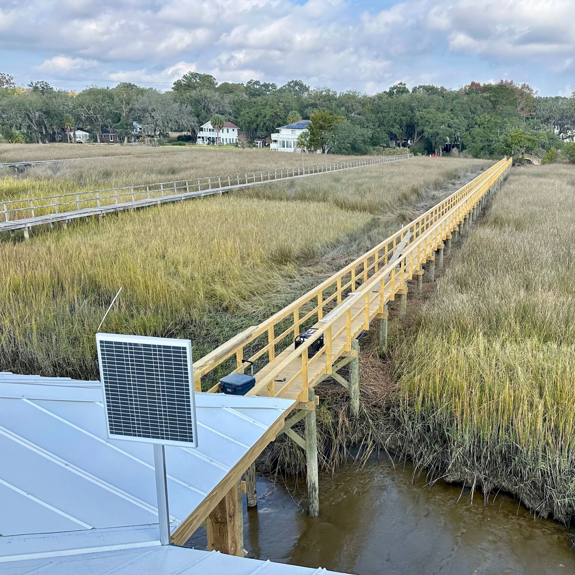 Long yellow walkway over marshland with a solar panel in the foreground