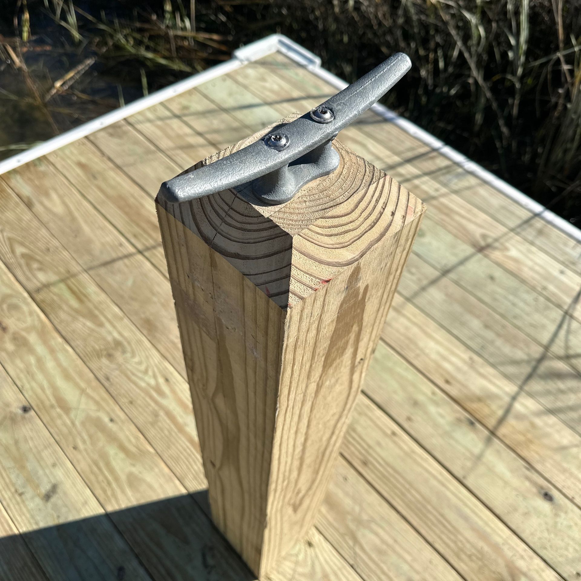 Metal mooring cleat mounted on a weathered wooden post on a sunlit dock